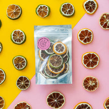 Load image into Gallery viewer, Lemon &amp; lime mix in a small pouch on a yellow and pink background with slices of dehydrated lemons and limes arranged around it.
