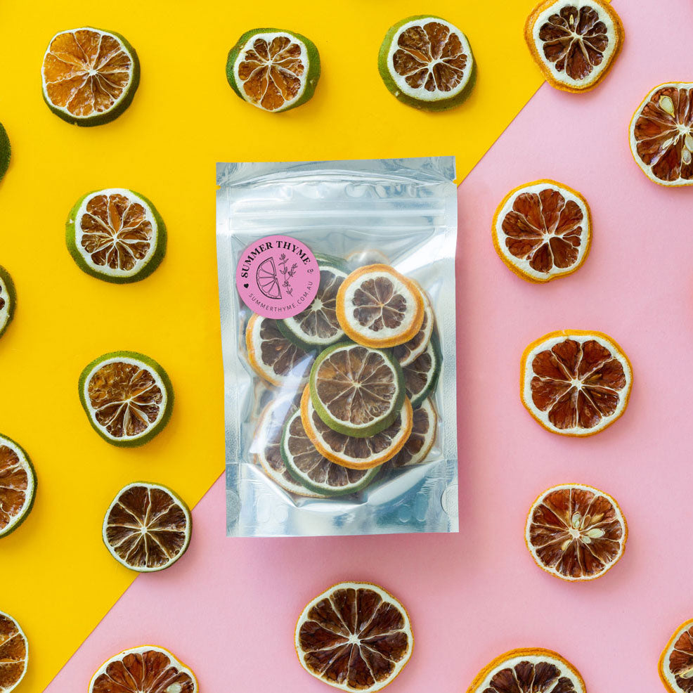 Lemon & lime mix in a small pouch on a yellow and pink background with slices of dehydrated lemons and limes arranged around it.