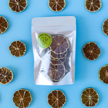 Load image into Gallery viewer, Slices of dehydrated limes arranged around a small pack of dehydrated limes on a light blue background.
