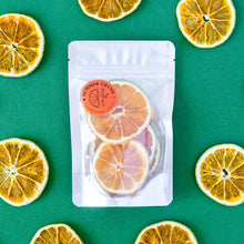 Load image into Gallery viewer, A small pack of dehydrated Valencia Oranges on a green background with dehydrated orange wheels arranged around it.
