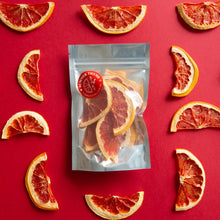 Load image into Gallery viewer, Dehydrated Ruby Red Grapefruit half-wheels arranged on a red background around a small pack of Summer Thyme Co. dehydrated ruby red grapefruits.
