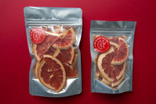 Load image into Gallery viewer, A large and a small pack of Summer Thyme Co. dehydrated ruby red grapefruits arranged next to each other on a red background.
