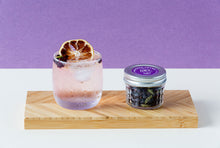Load image into Gallery viewer, Stylised photo of a cocktail in a short glass with some botanicals and a slice of dehydrated lemon. Next to it is a jar of G&amp;T botanicals mix - gin and tonic garnish mix.
