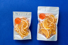 Load image into Gallery viewer, Two bags of dehydrated orange half-wheels - one small, one large, arranged next to each other on a dark blue background.
